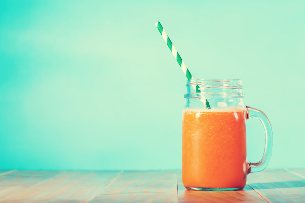 Carrot juice in masons jar on light blue green background